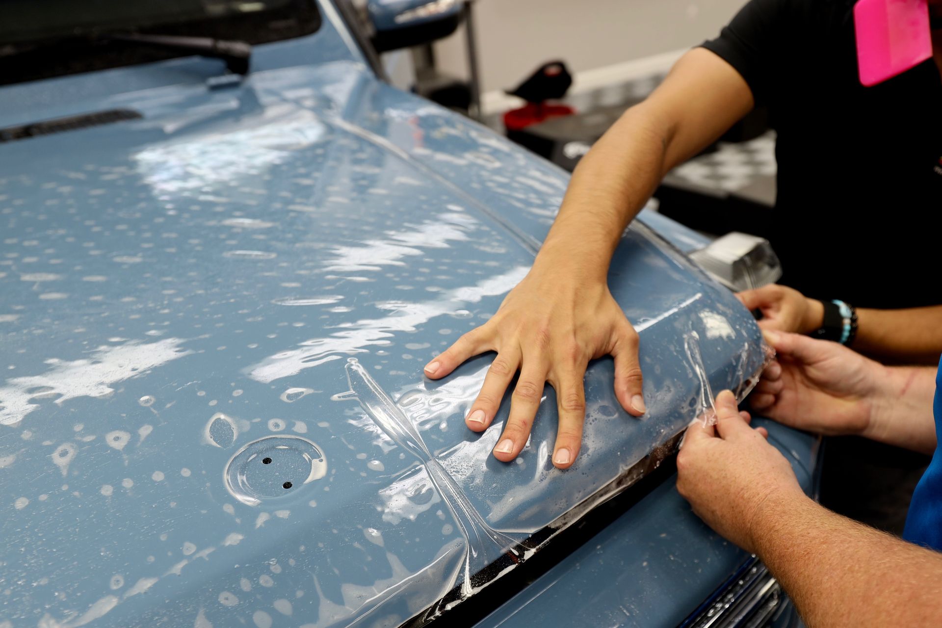 A man and a woman are applying a protective film to the hood of a car.