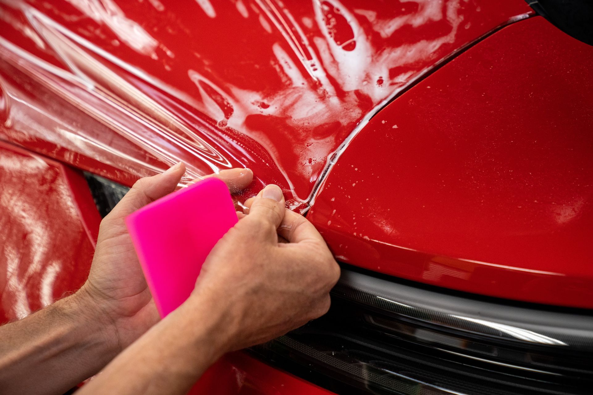 A person is wrapping a red car with a pink sponge.