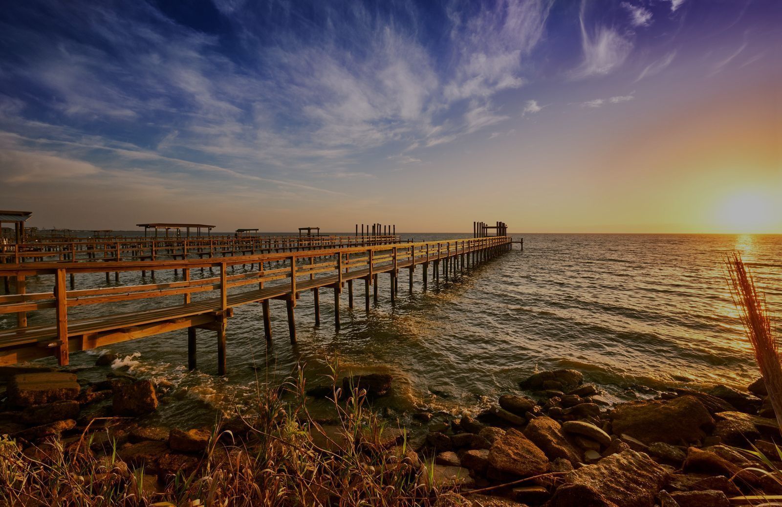 Sunset over a wooden pier stretching into choppy water under a dramatic sky