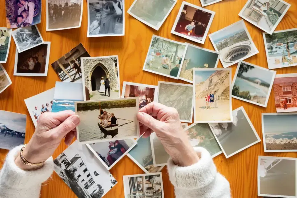 Hands holding a vintage photo over a scattered spread of old photographs on a wooden table