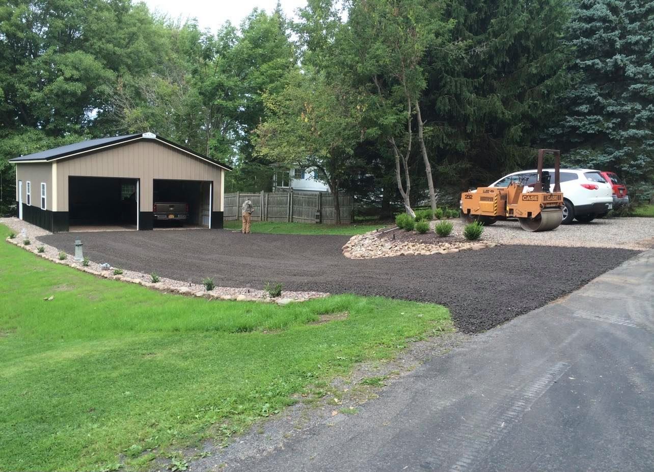 Asphalt driveway and garden area with a garage and vehicles.