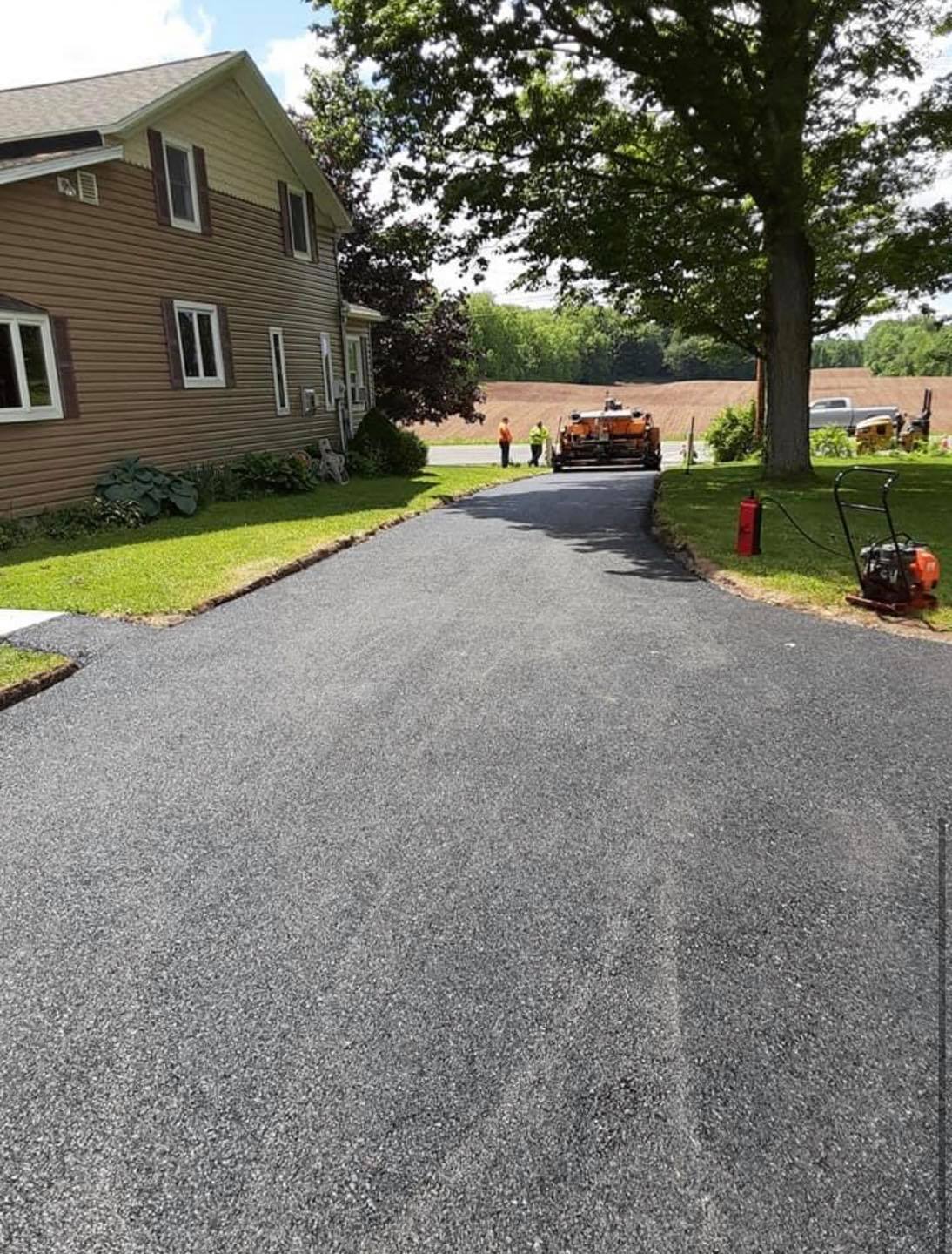 Asphalt driveway being paved; house and equipment visible.