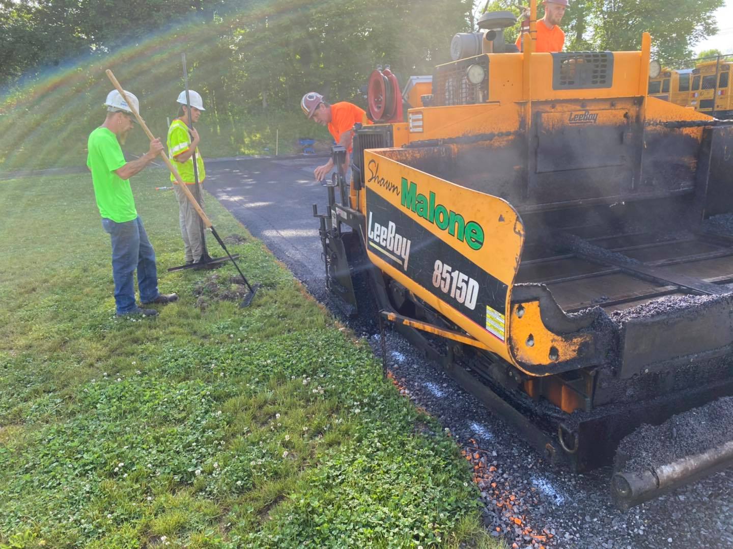 Road crew paving asphalt with machinery. Workers in safety vests and green shirts.