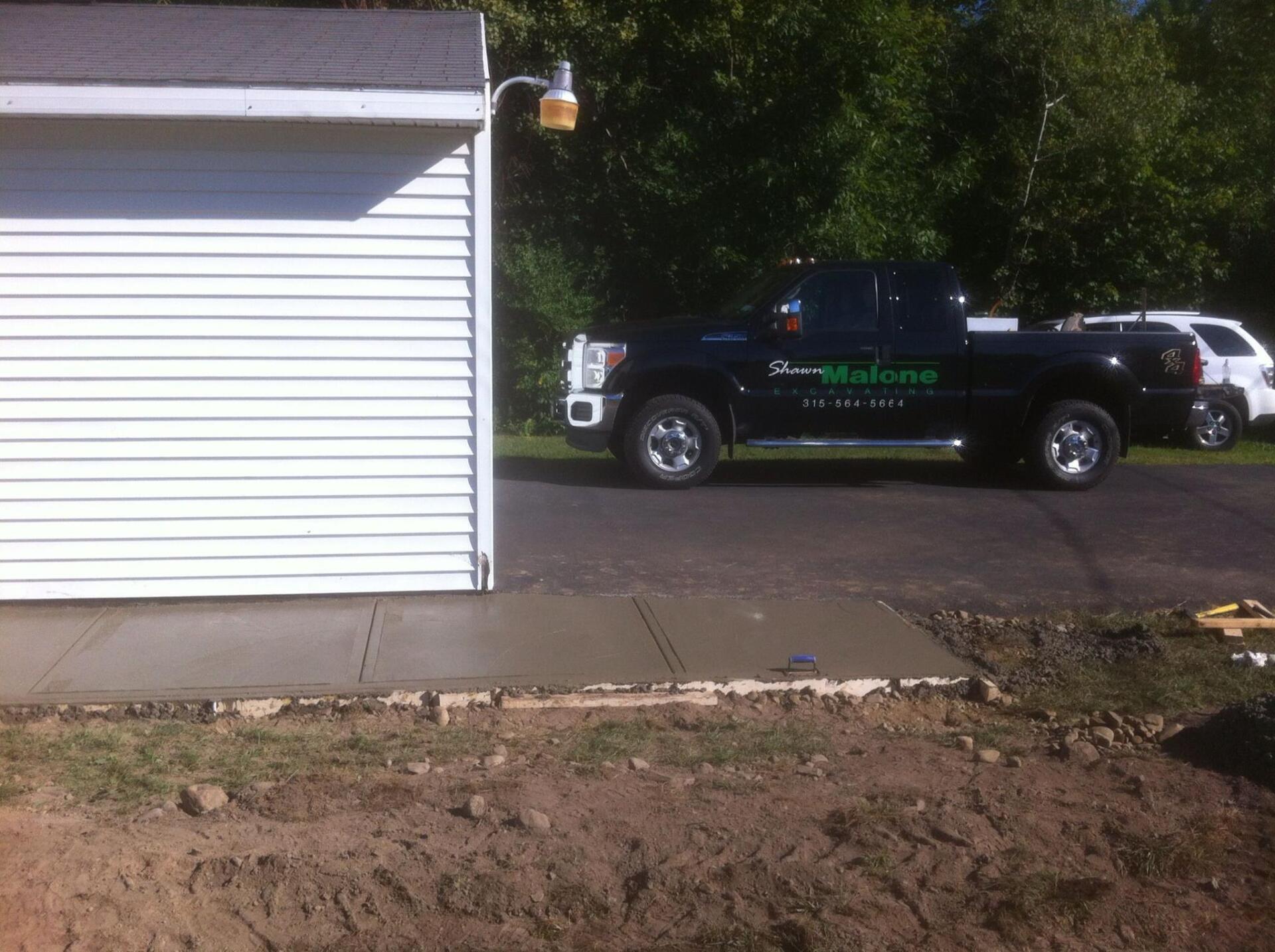 New concrete pad next to a white garage, black truck parked on a driveway.