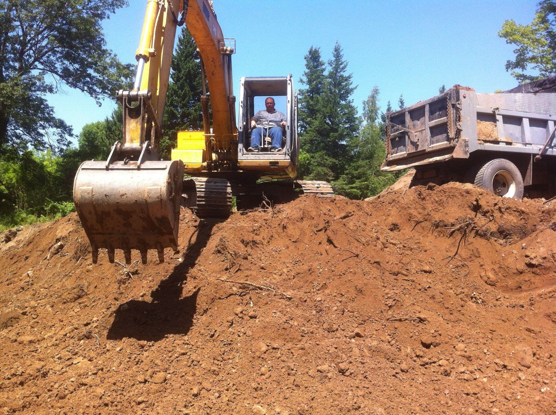 Excavator loading dirt into a dump truck on a sunny day.