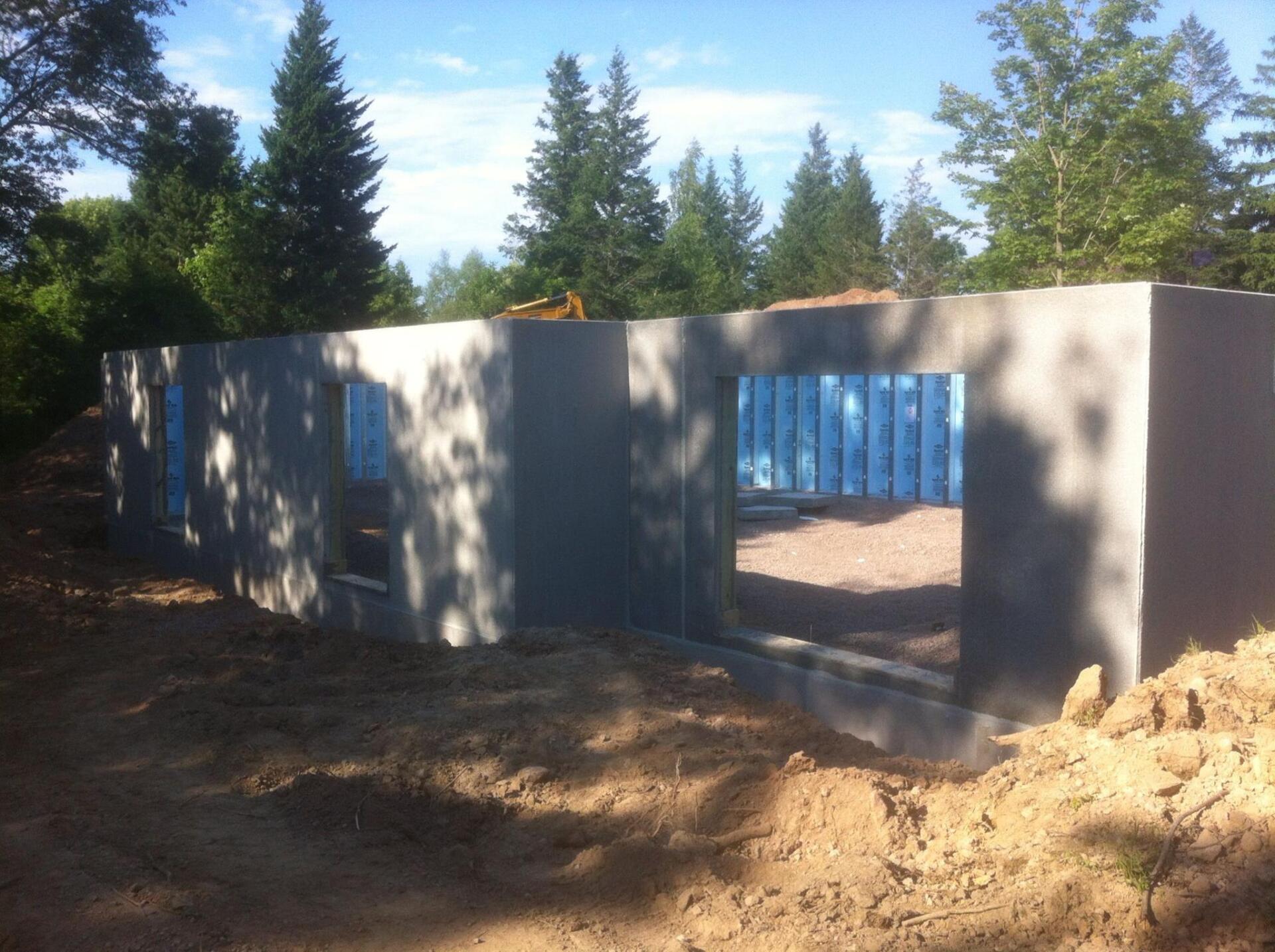 Exterior concrete foundation walls with window openings under construction, surrounded by dirt and trees.