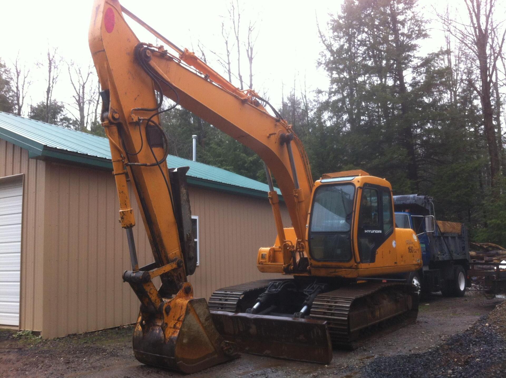Yellow excavator parked near a tan building and truck.