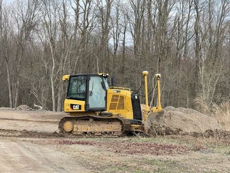 Yellow Caterpillar bulldozer plowing dirt, near trees.