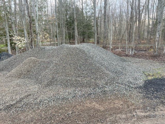Pile of gray gravel on the ground, trees in the background.