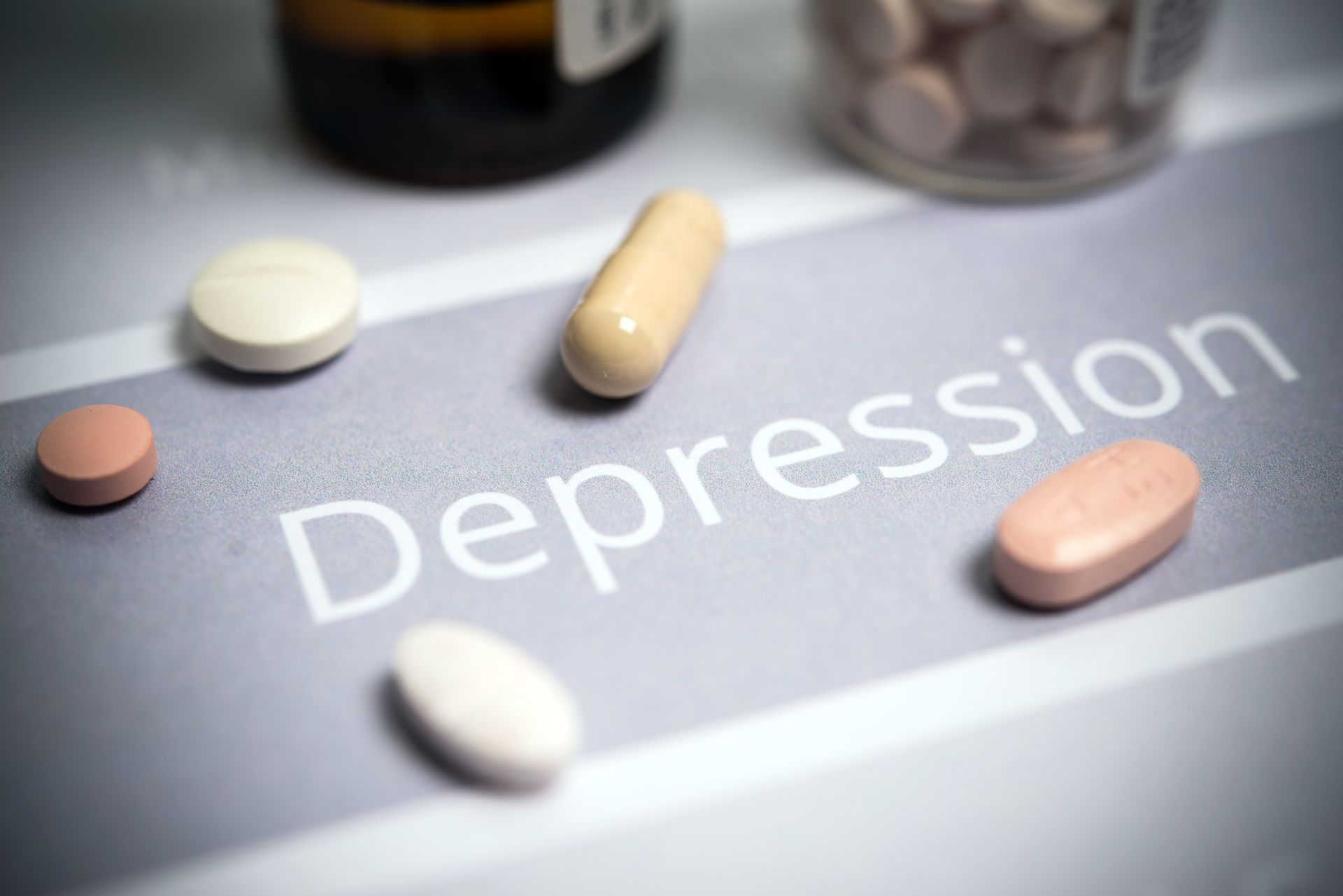Pills scattered around the word “Depression” on a gray surface
