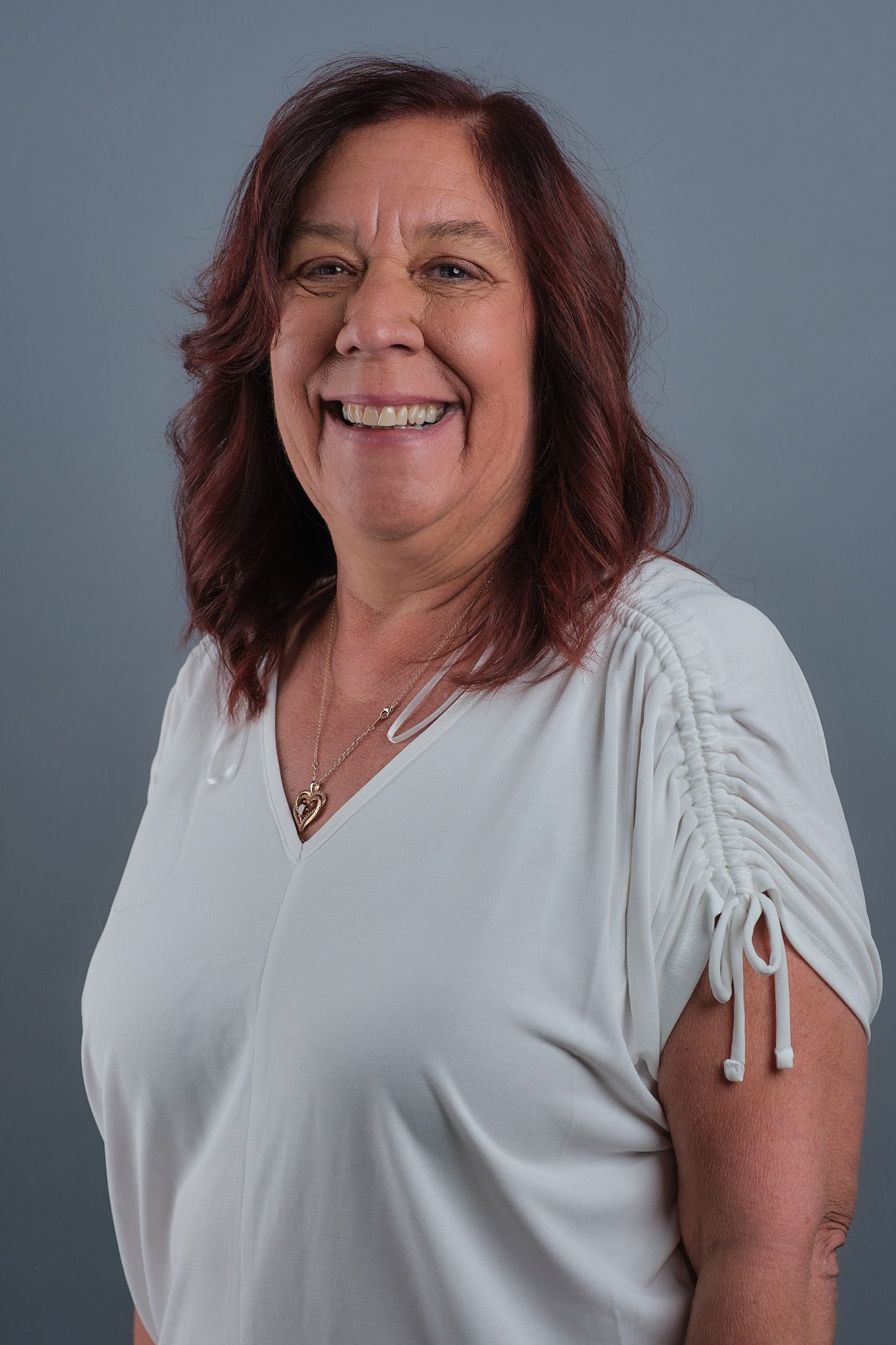 A woman with red hair is wearing a white shirt and smiling.
