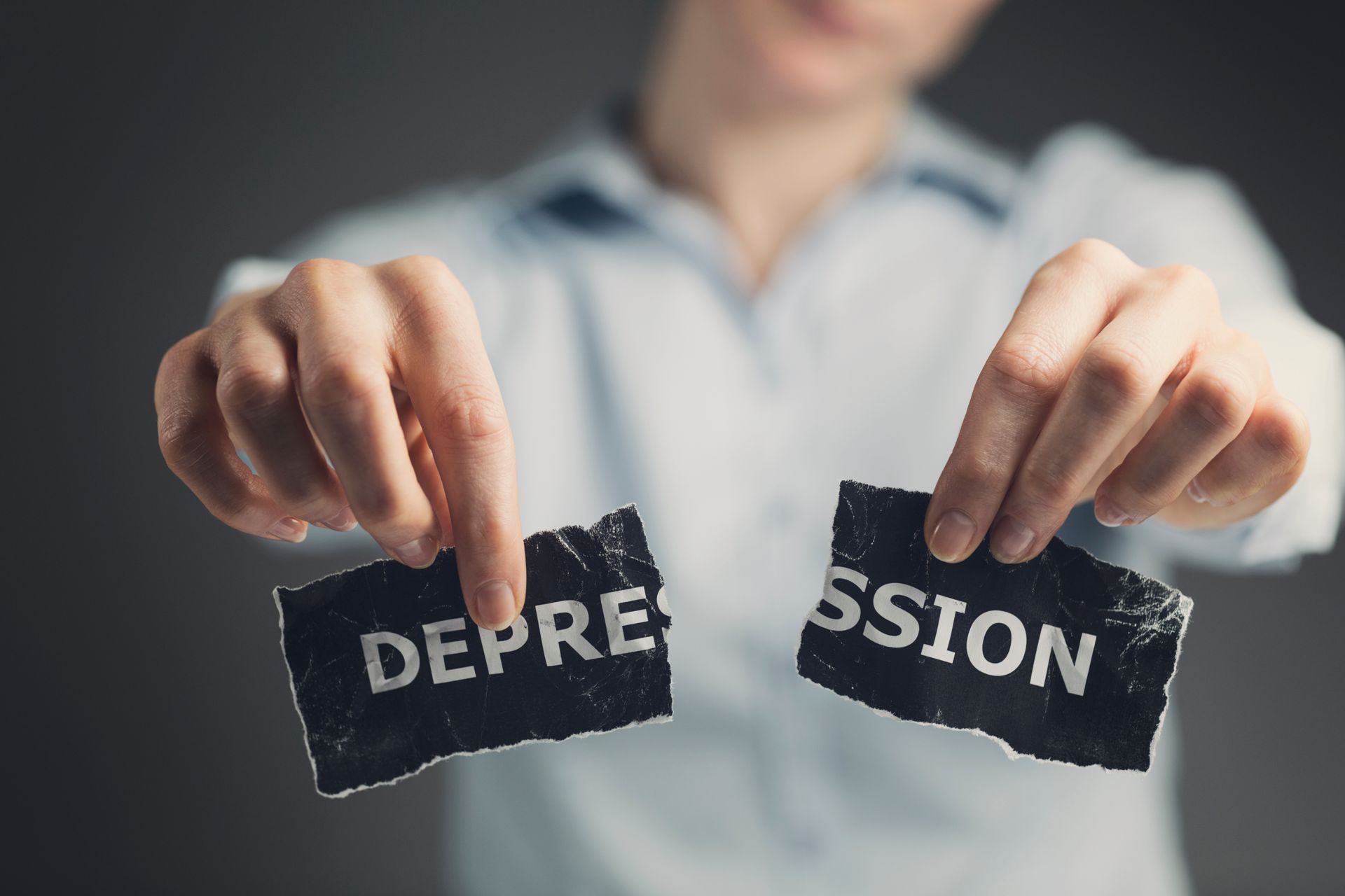 Hands tearing a black paper labeled “DEPRESSION” in front of a blurred person
