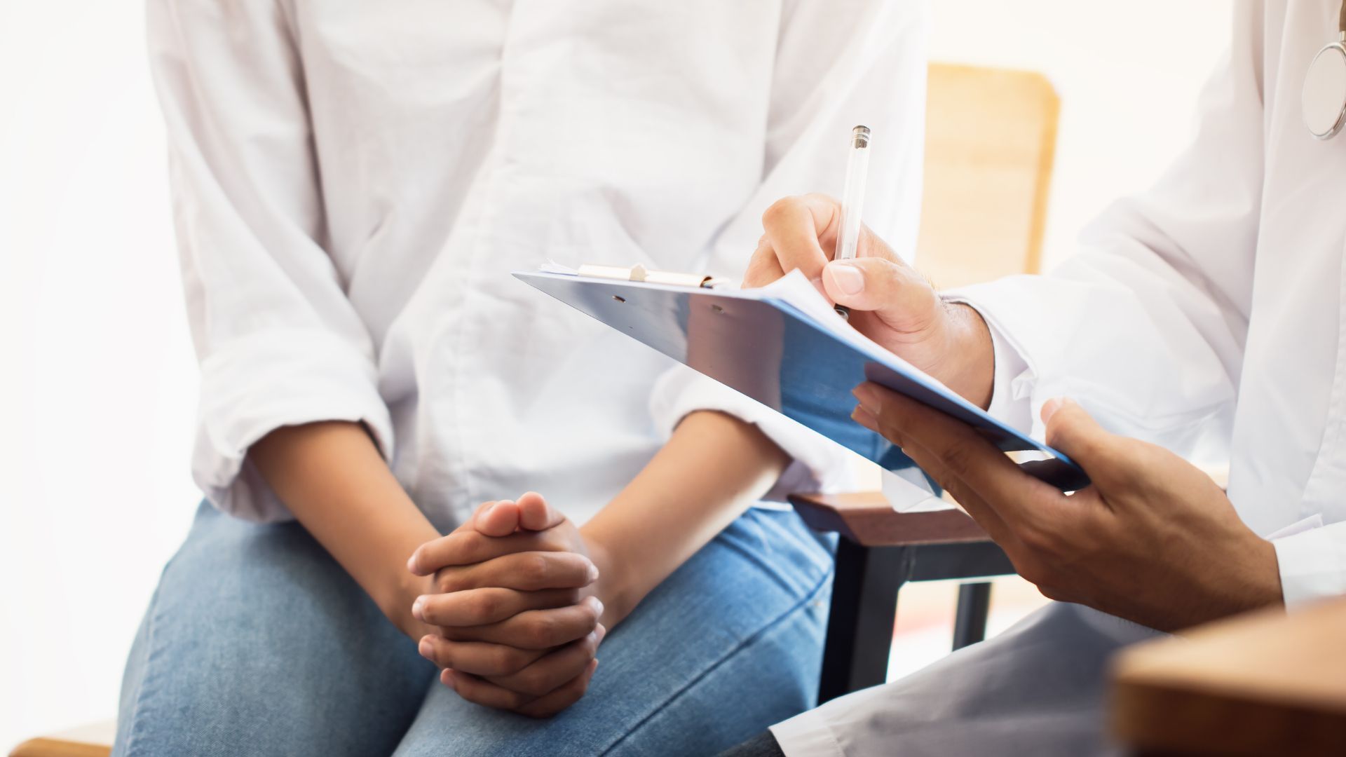 Clinician taking notes while speaking with a seated patient in a bright office