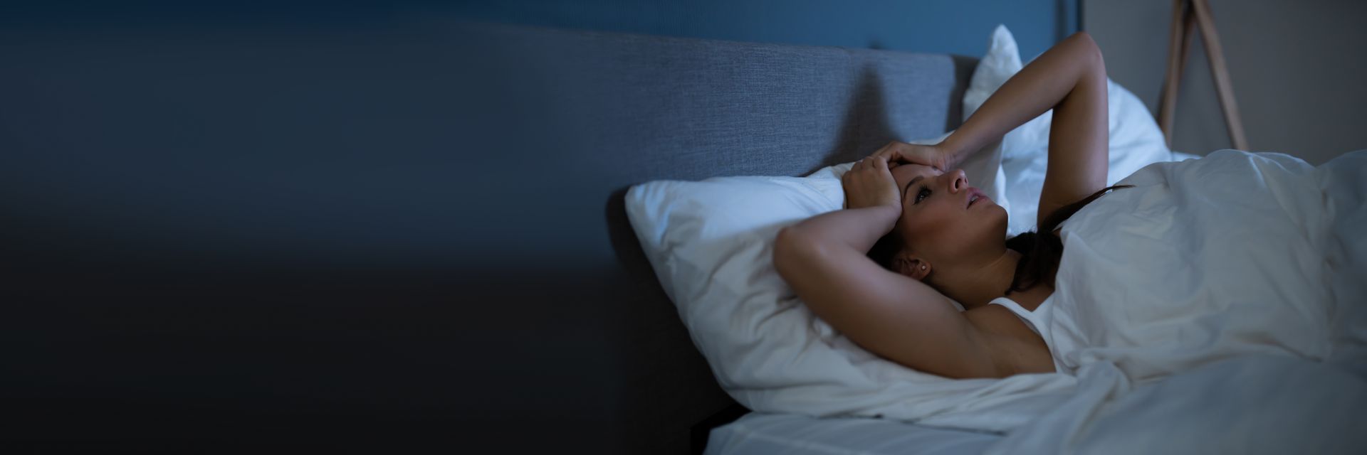 Person lying in bed at night, holding her head.