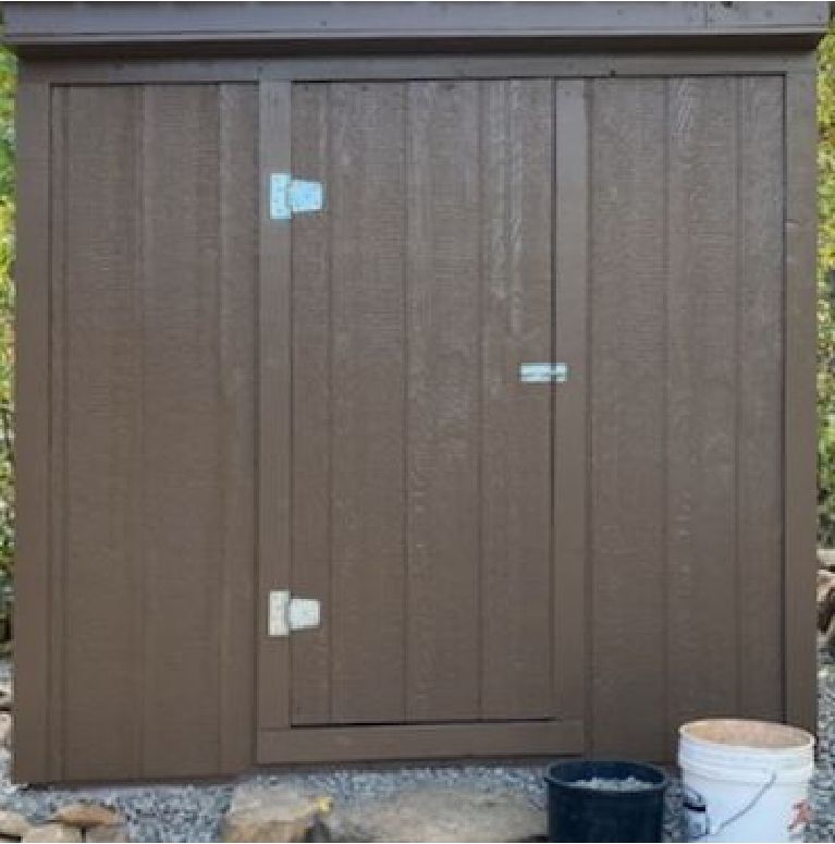 Brown garden shed with a small door and a couple of buckets beside it