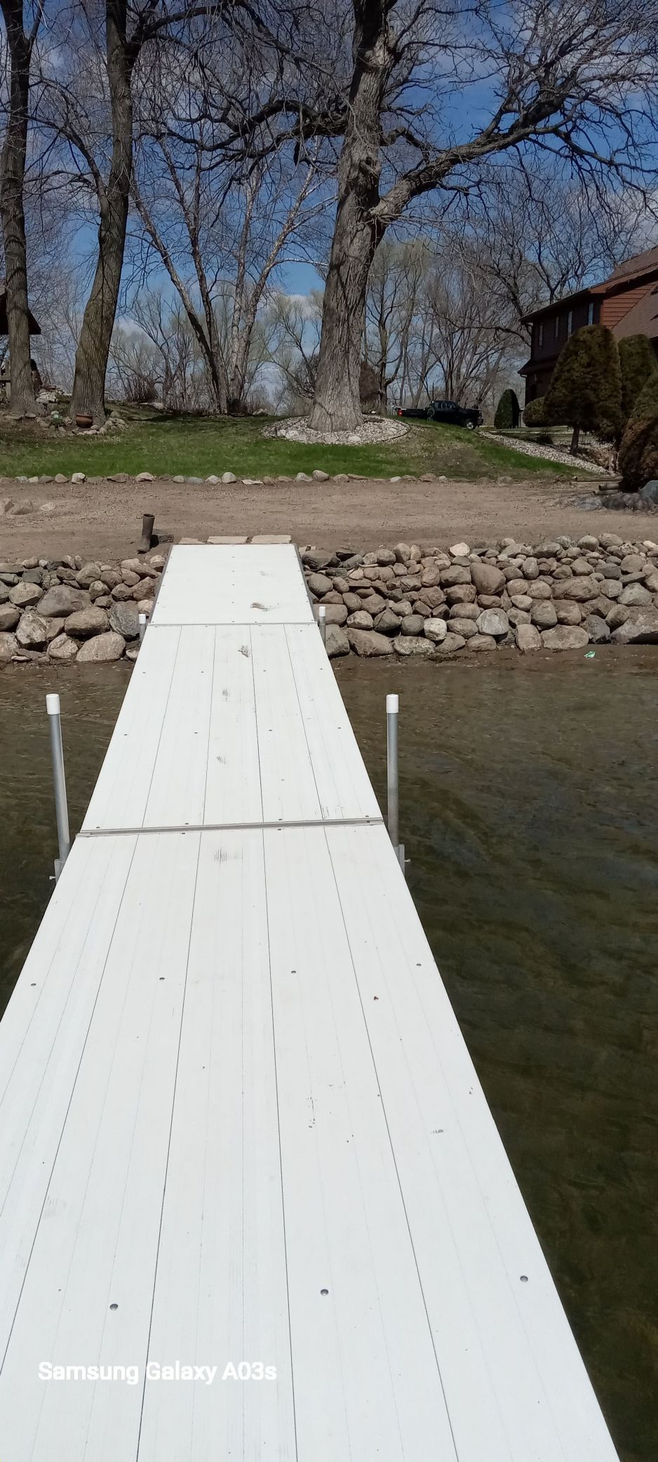 White dock leading to a rocky shoreline with trees under a blue sky