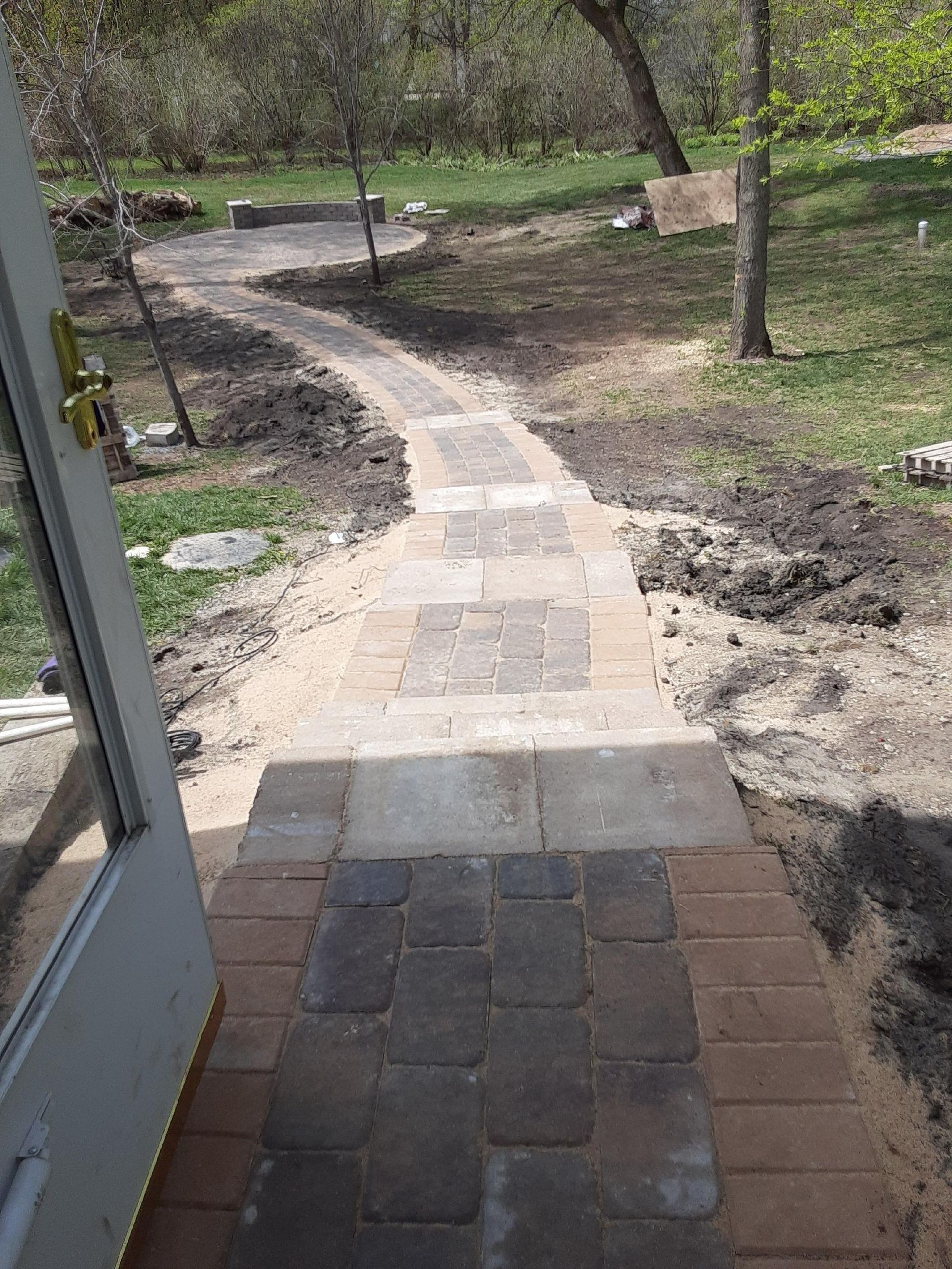 Stone-and-brick path curving through a wooded yard, viewed from a doorway.