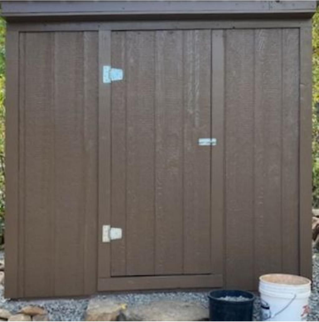 Brown wooden shed door with three metal latches and a bucket beside it