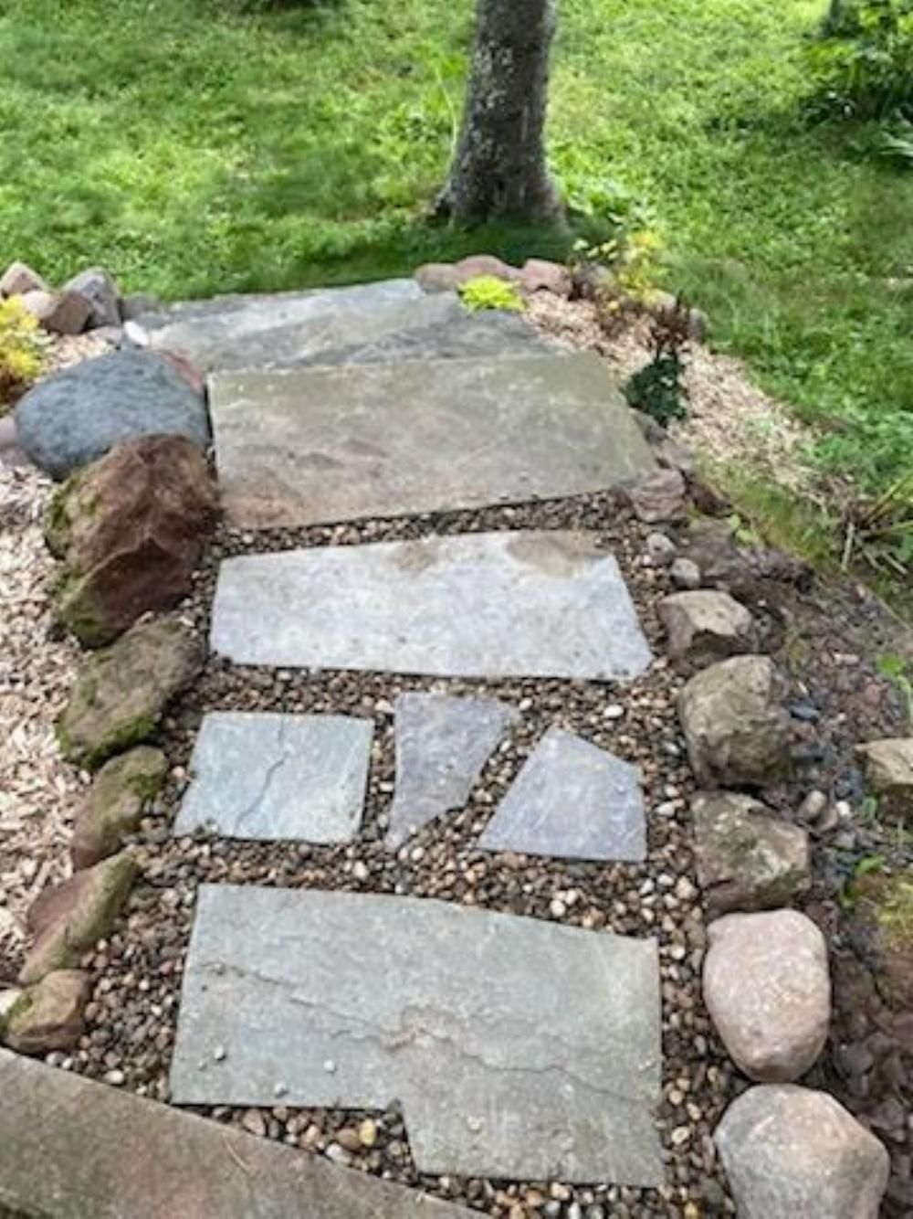 Stone garden path with irregular stepping stones and rocks beside grass and a tree