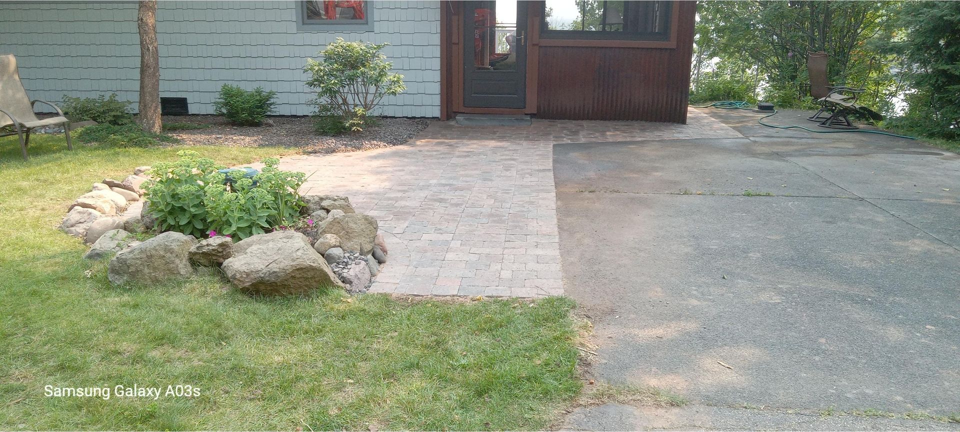 Front yard with stone-bordered flower bed, driveway, and house entrance with a brown door and garage