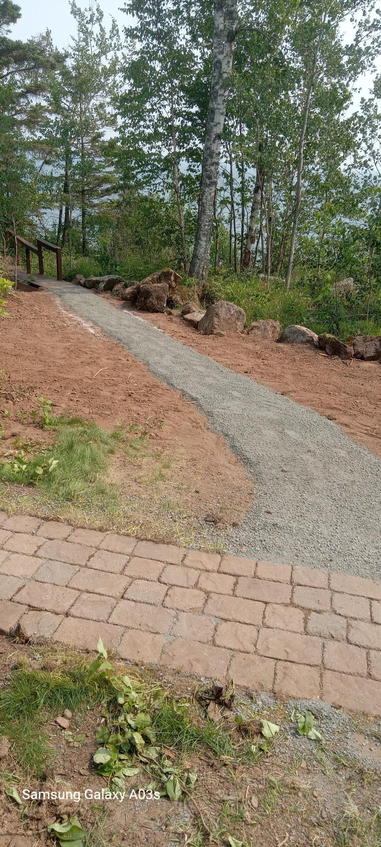 Gravel path curving through a wooded garden beside a brick patio and mulch-covered slope