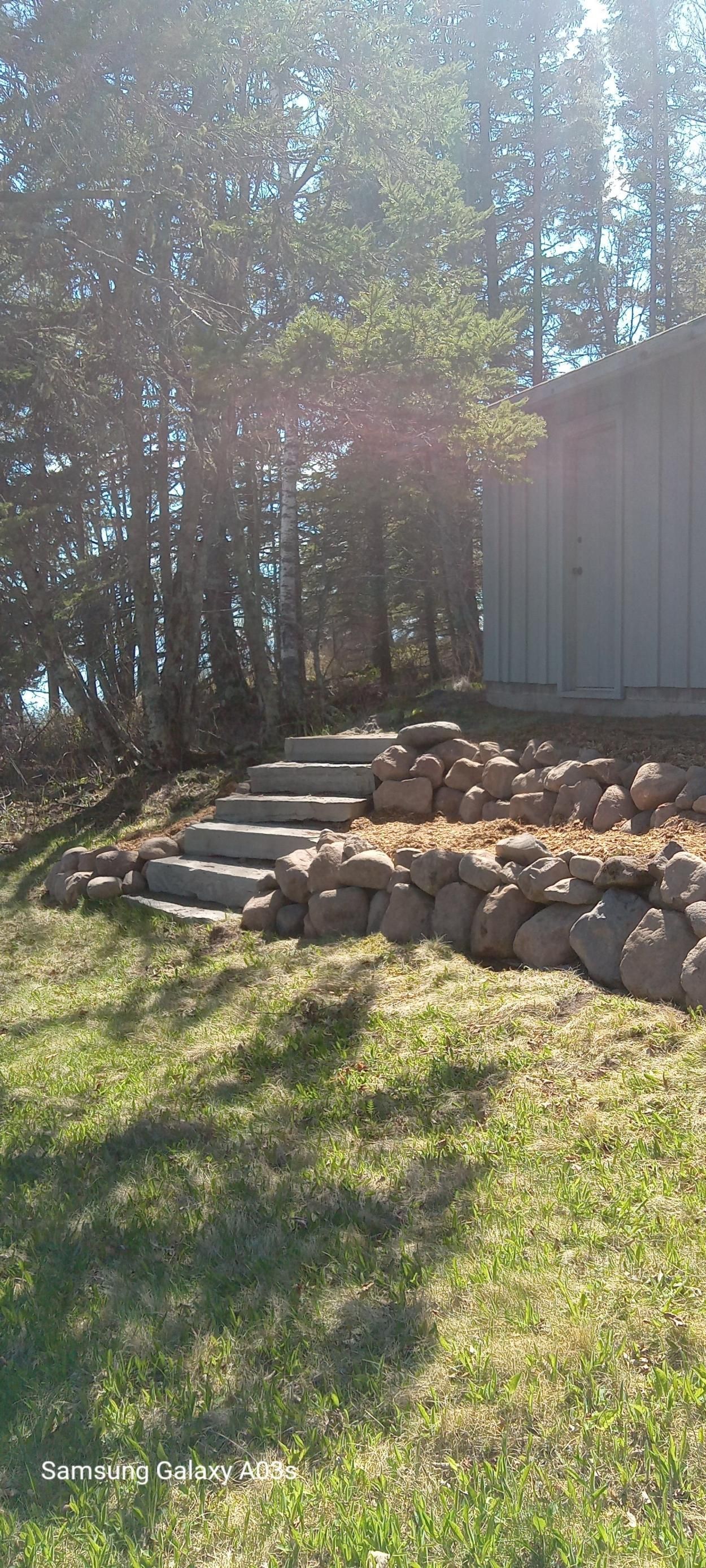 Stone steps leading to a gray shed beside a sunlit grassy yard and trees