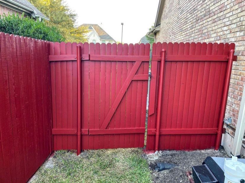 Red wooden backyard gate with diagonal brace between red fences and a grass path.