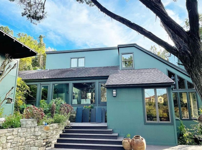 Modern teal house with steps, large windows, and a tree in the foreground