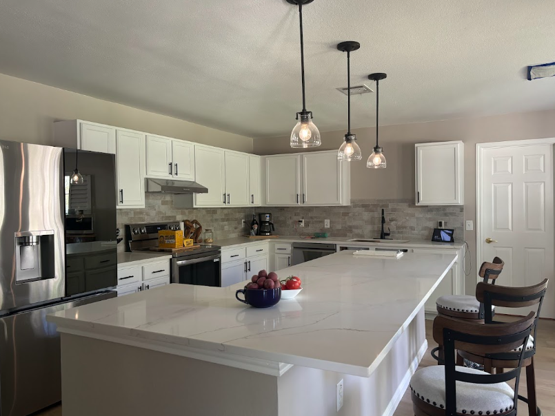 Modern white kitchen with large island, pendant lights, stainless appliances, and bar stools by the counter