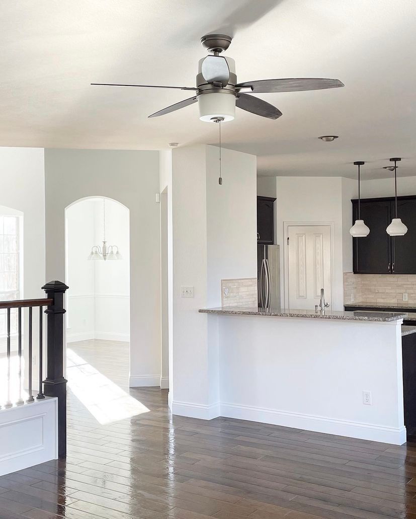 Bright open kitchen and living area with white walls, dark wood floors, and ceiling fans