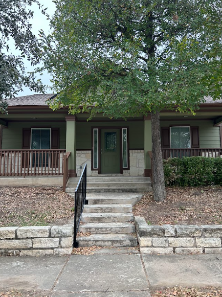 Front view of a house with front steps, porch, and a large tree in the yard.