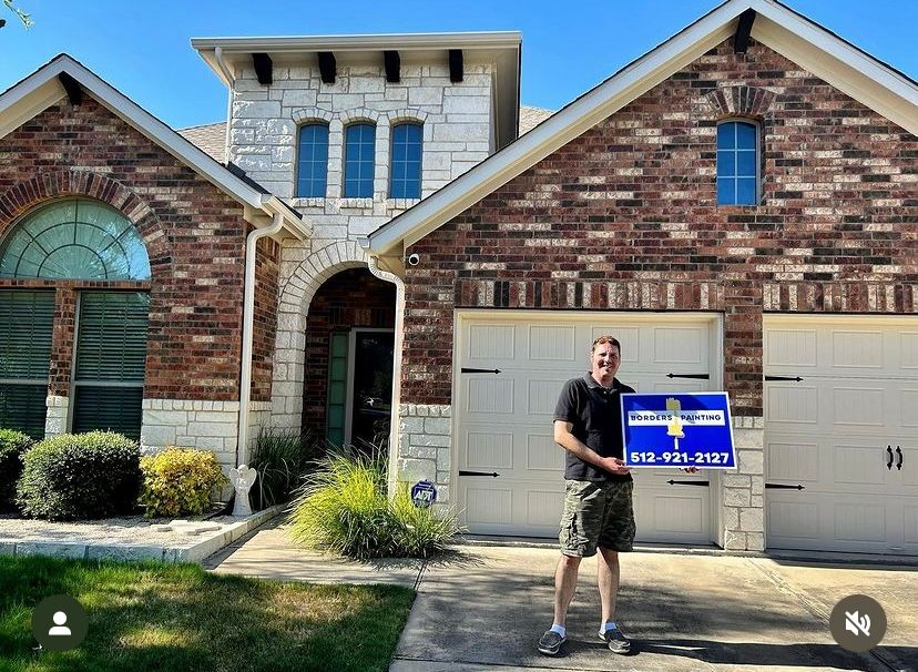 Man holding a sign in front of a brick suburban house with a two-car garage.