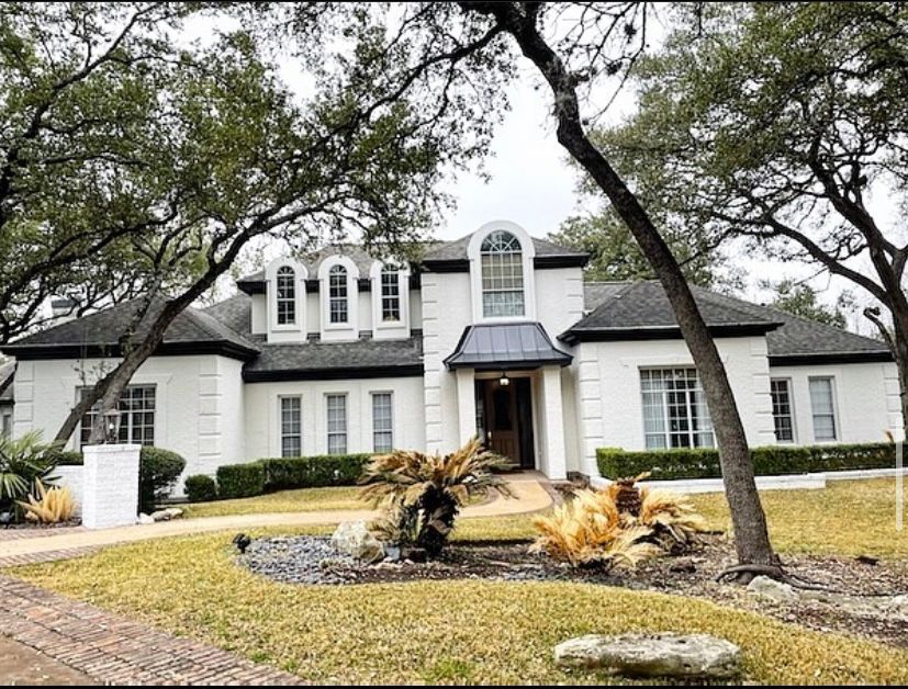 Large white two-story house with black shutters, arched windows, and a landscaped front yard with trees