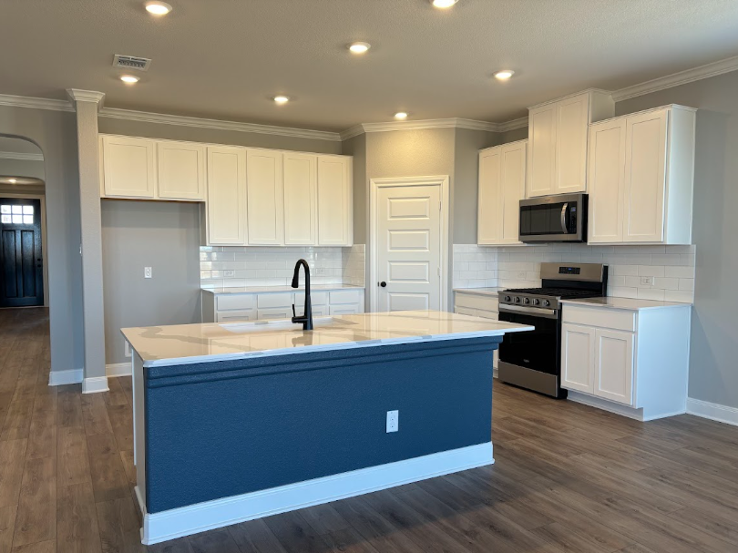 Modern kitchen with white cabinets, stainless appliances, and a blue island with a white countertop