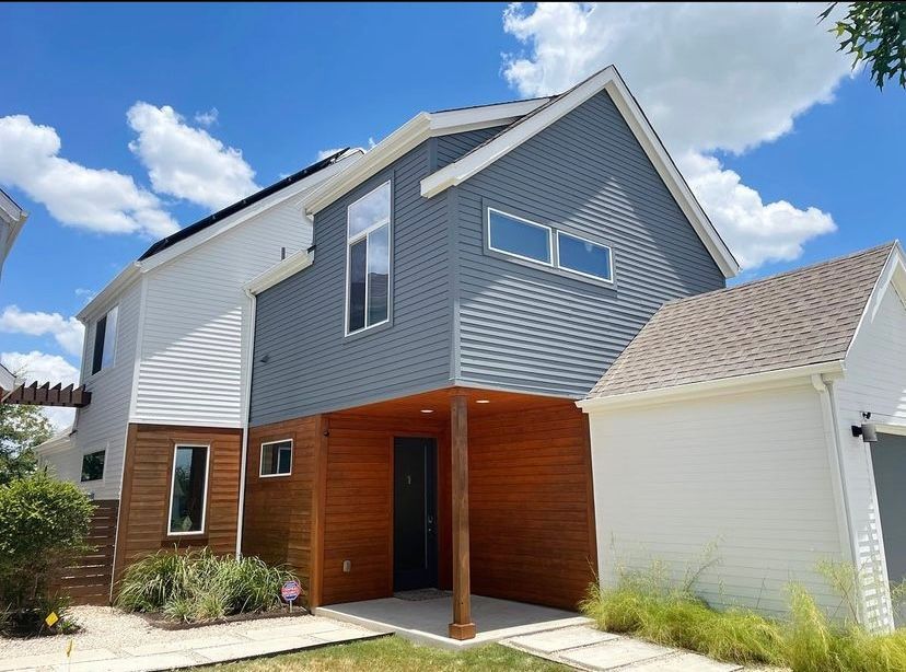 Modern two-story house with gray siding, wood accents, and a white garage under a blue sky