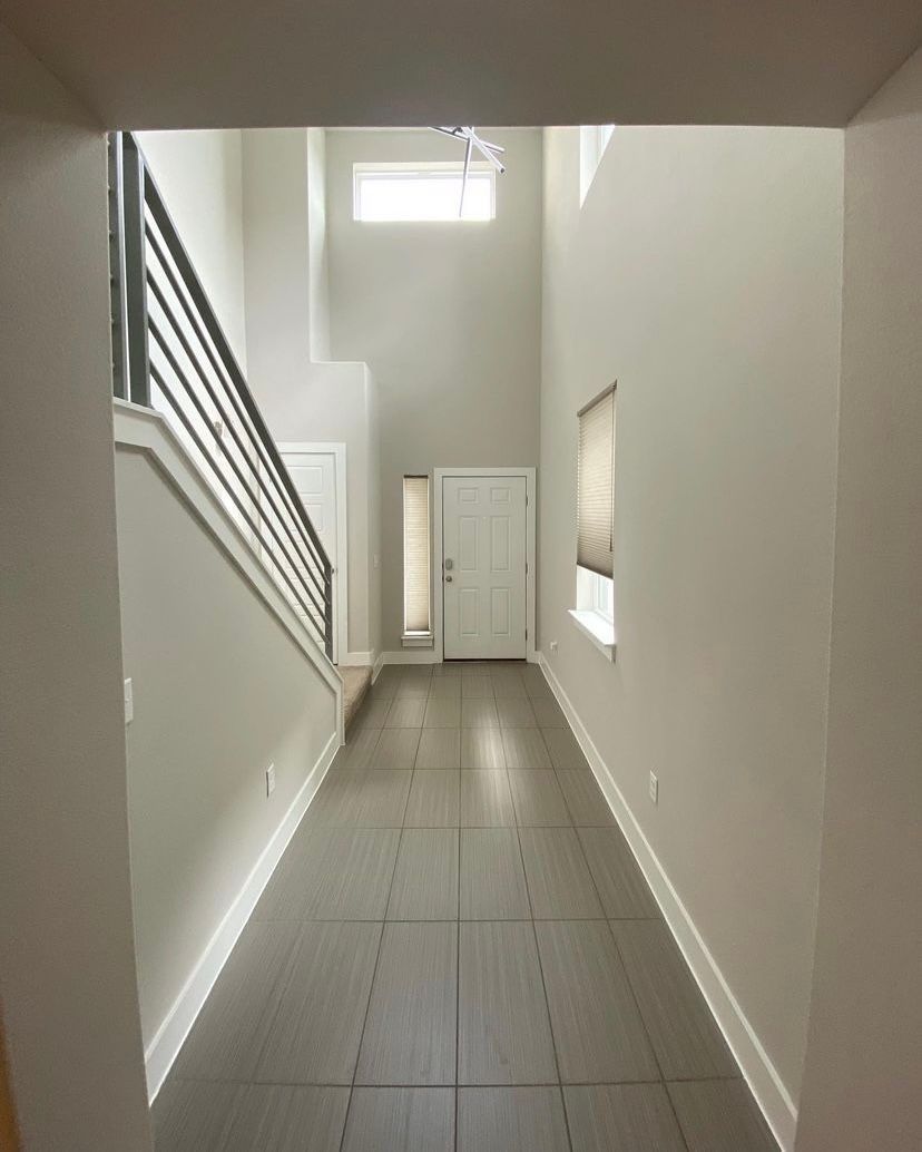 Empty modern hallway with gray tile floor, white walls, staircase, and a small window at the end.