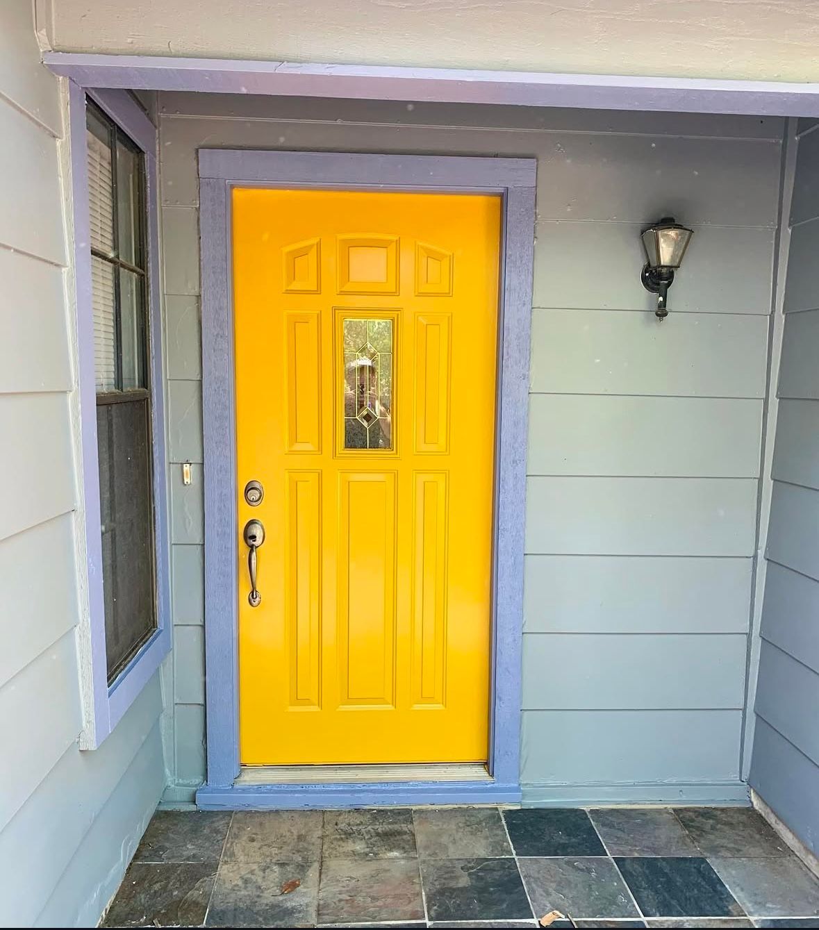 A yellow door on a gray house with a purple trim