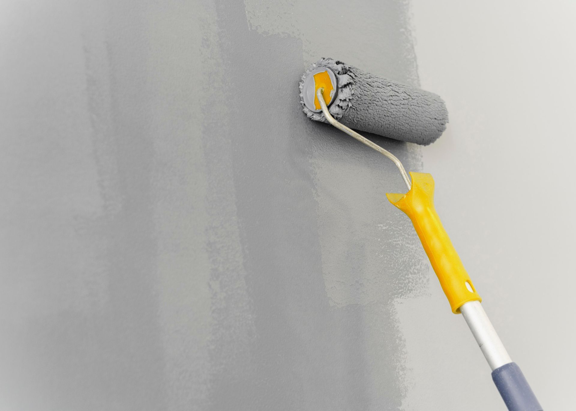 Paint roller applying grey paint to a wall.