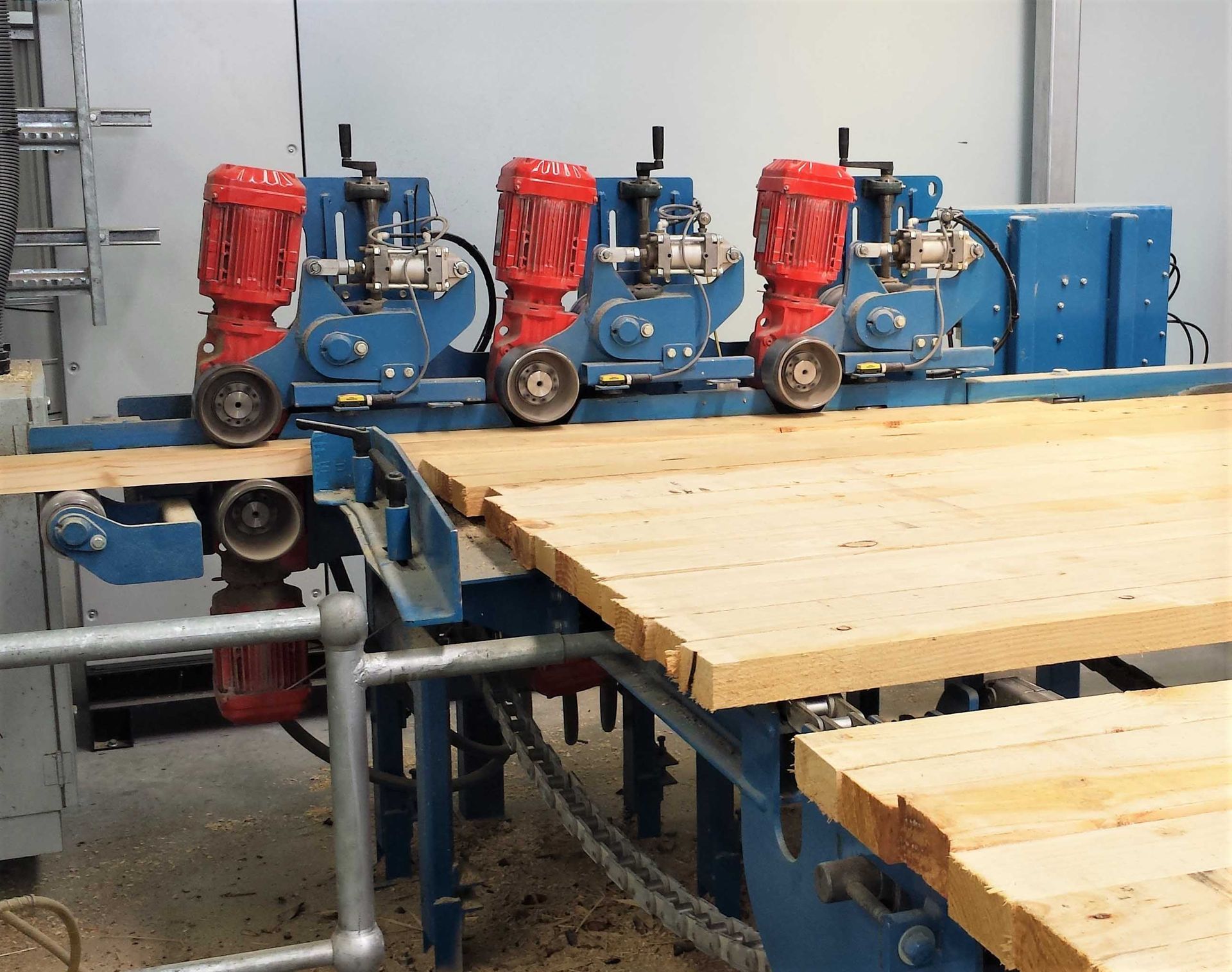 Lumber processing machine with four red-motorized cutting heads smoothing a wooden board.