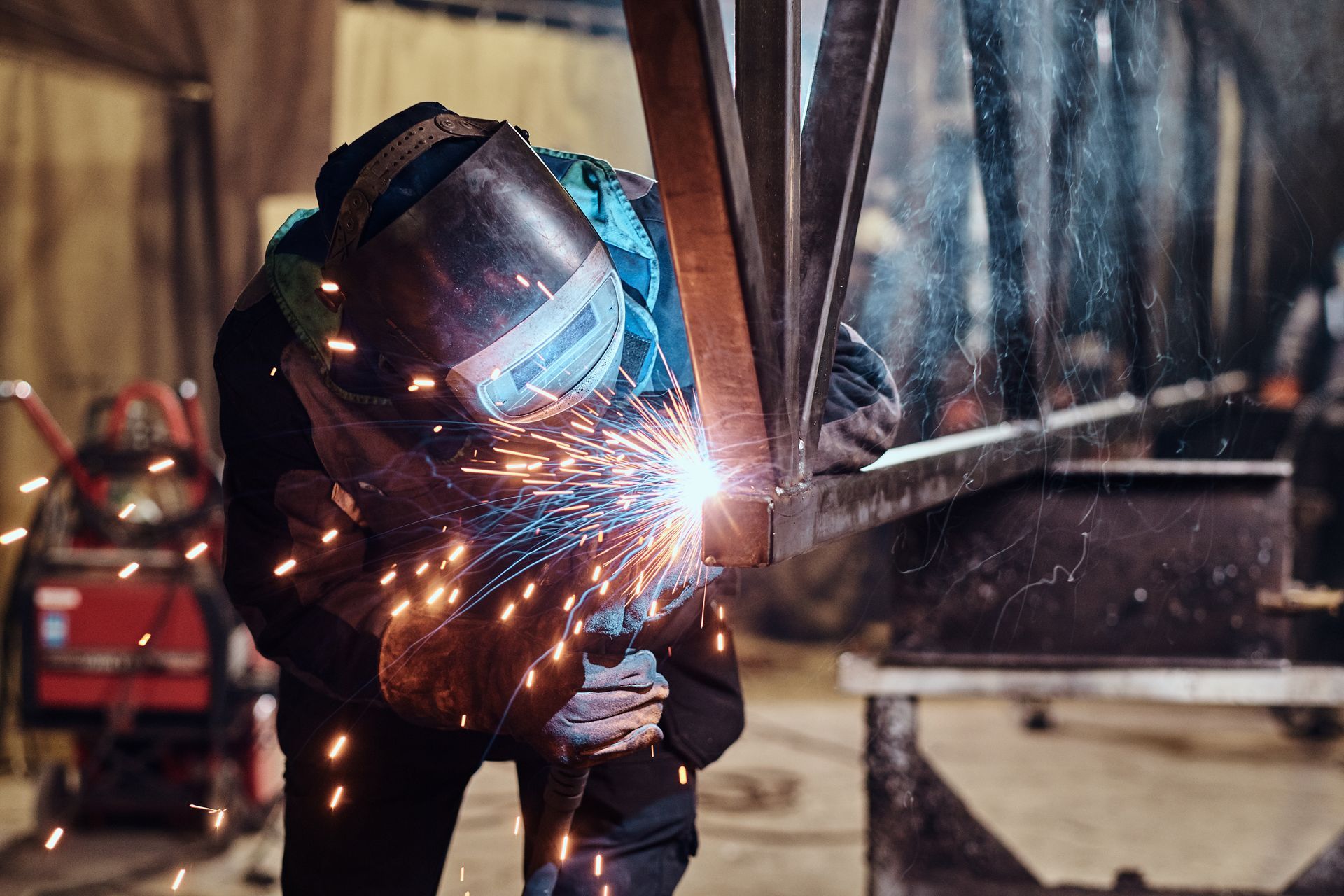 A worker is working at a custom engineering workshop, welding a piece of rail using special tools.