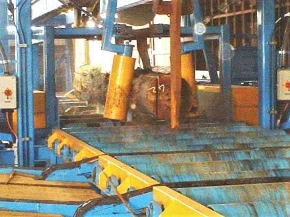 A large machine with blue and yellow parts cutting a log in an industrial setting.