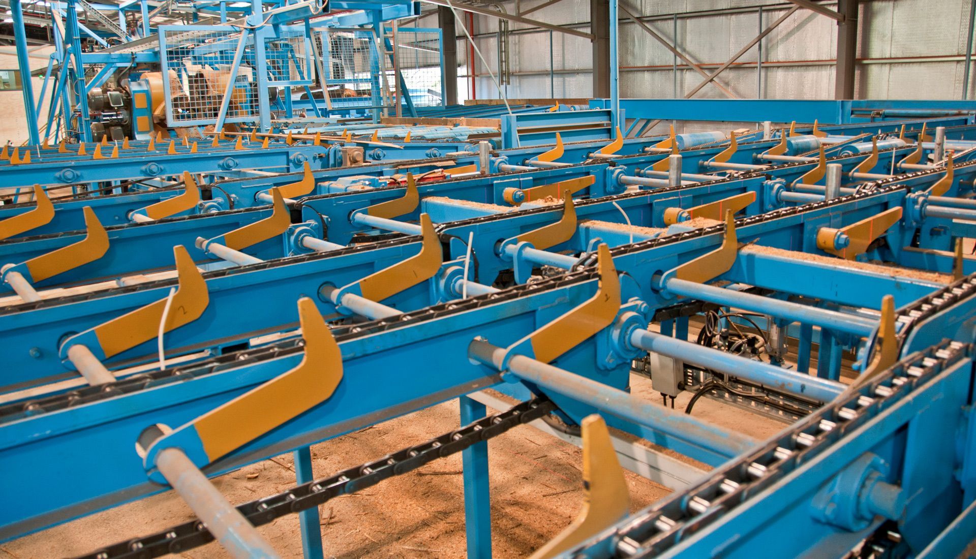 Blue industrial conveyor system with yellow angled arms in a factory setting.