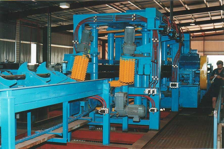 Blue industrial machine with brush-like rollers in a factory setting. A person stands nearby.