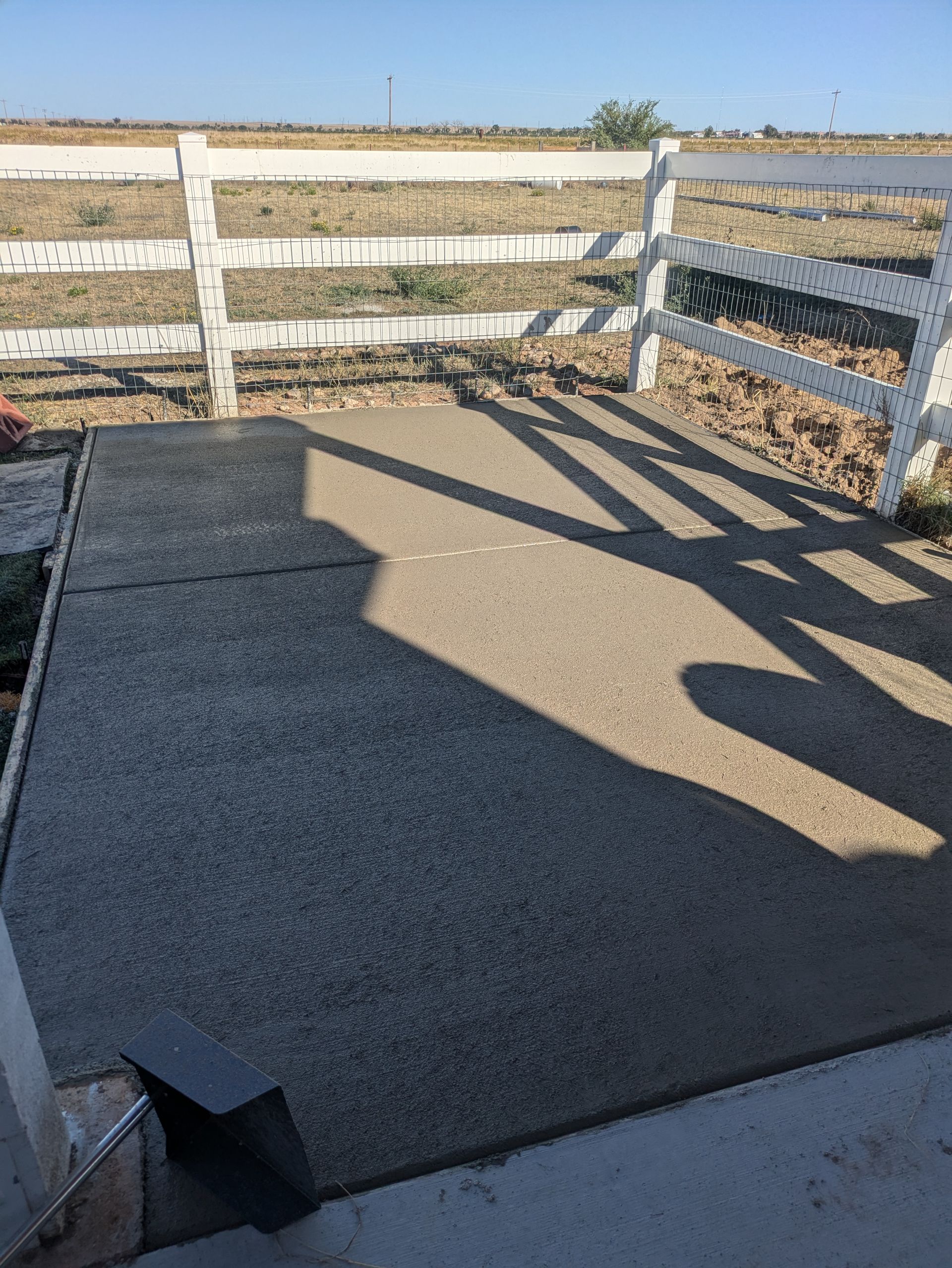 A shadow of a fence is cast on a concrete surface.
