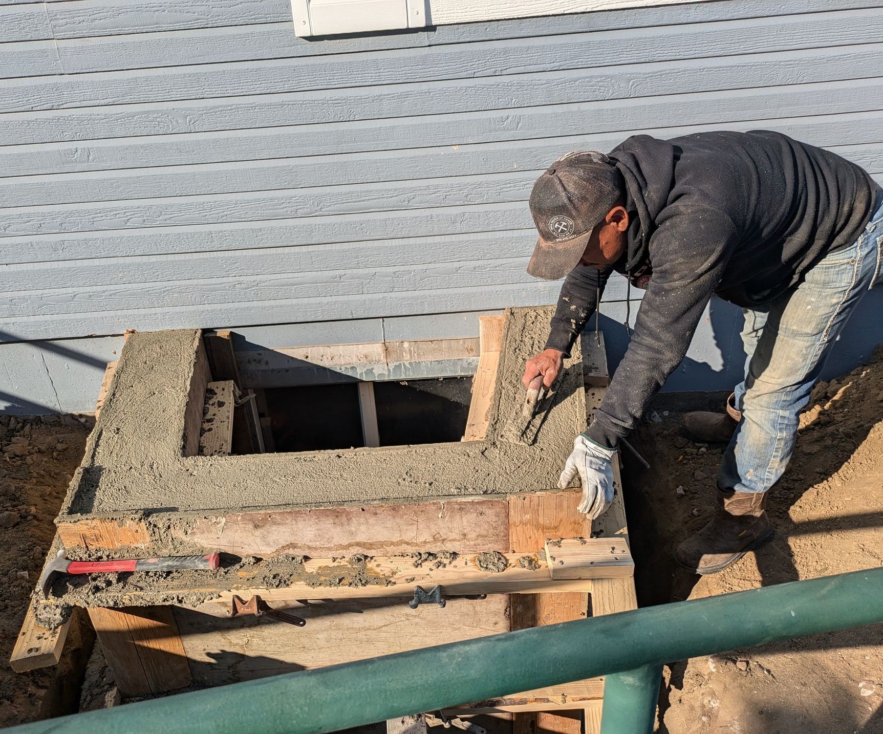 A man is working on a hole in the ground in front of a house.