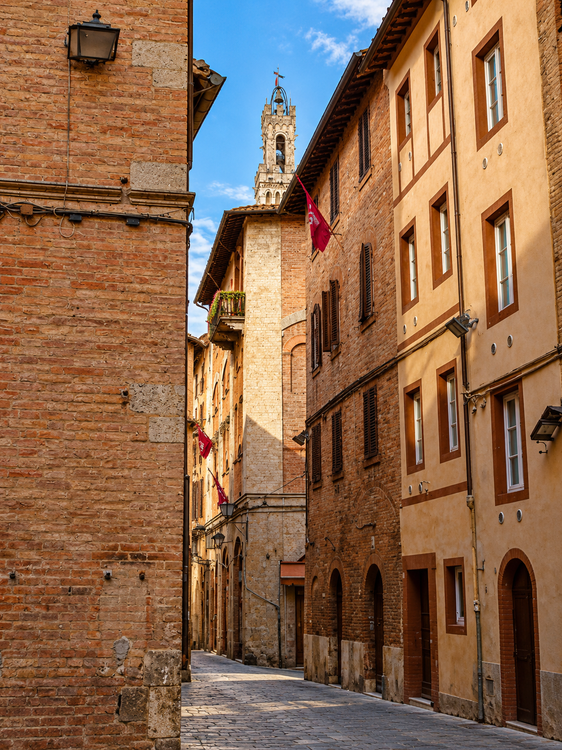 Stretta strada acciottolata, fiancheggiata da vecchi edifici in mattoni, in un centro storico dai colori caldi