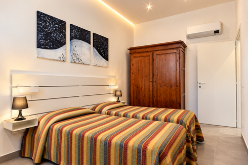 Accogliente camera da letto con copriletto a righe, armadio in legno, quadri alle pareti, lampada da comodino e aria condizionata