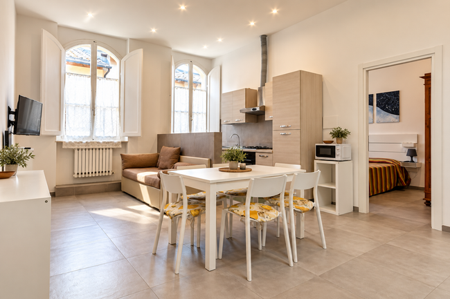 Luminosa cucina-sala da pranzo open space con tavolo e sedie bianchi, divano beige e finestre ad arco