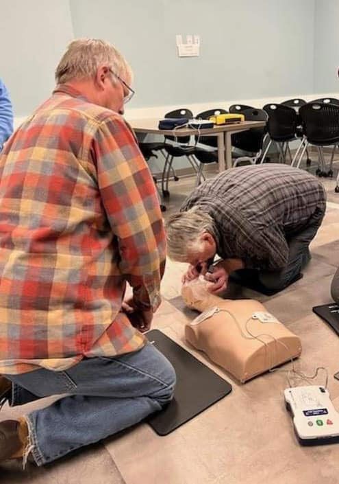 Two men are kneeling on the floor looking at a mannequin.