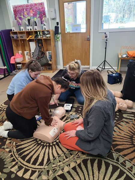 A group of people are kneeling on the floor and practicing on a mannequin.